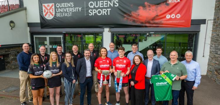 Large group of people gathered under Queen's Sport banner holding winning trophies